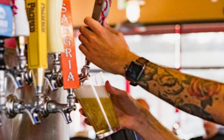 Bartender with wrist tattoo pouring a glass of beer.