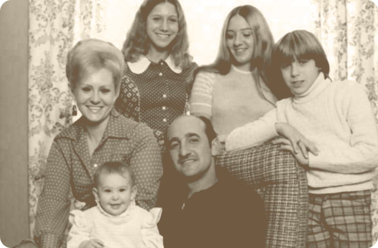 Vintage black and white photo of a family with a father, mother, two daughters, a son, and a baby in 1970s clothes