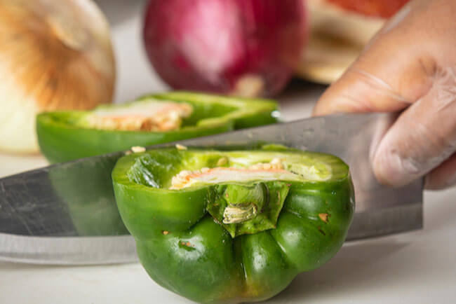 Picture of a green bell pepper being chopped in half by a large knife