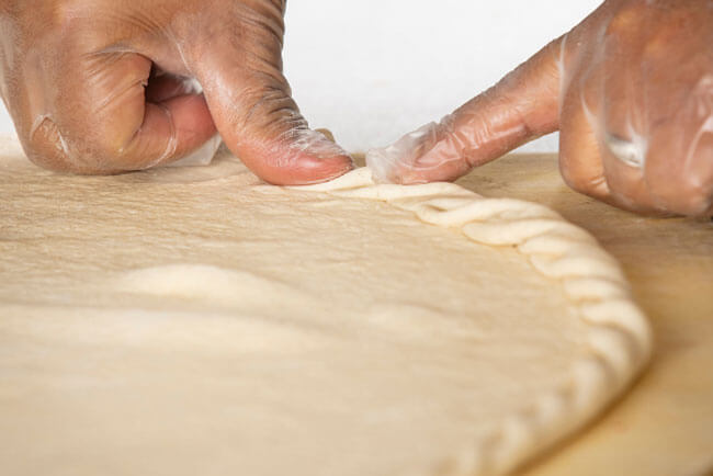 Hands press into specialty pizza dough to create a rigged crust