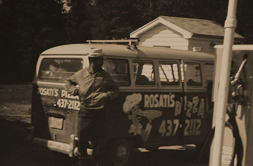 Vintage photo of a man standing in front of an old VW bus covered in Rosati's Pizza stickers
